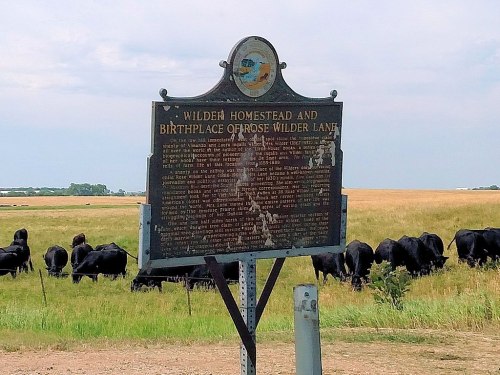 Historical marker for Wilden Homestead and birthplace of Rose Wilder Lane, with cattle grazing in the background.