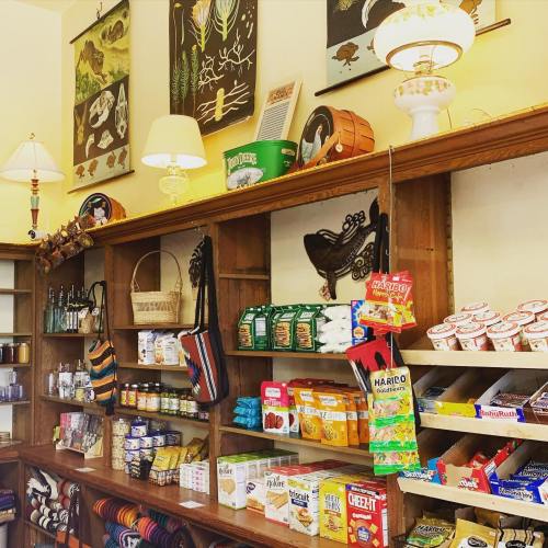 A cozy shop interior with wooden shelves displaying snacks, drinks, and decorative items, illuminated by lamps.