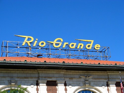 Sign reading "Rio Grande" in bold yellow letters against a clear blue sky, atop a historic building.