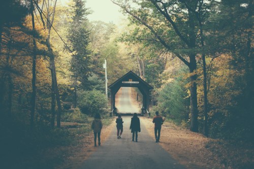 A group of five people walking towards a covered bridge surrounded by autumn trees.