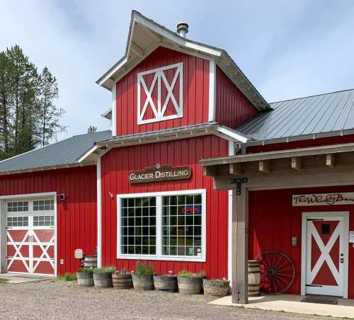 A red barn-style building with a sign for Glacier Distilling, surrounded by trees and gravel.