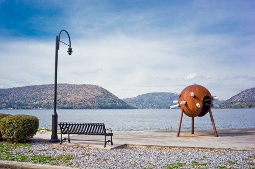 A scenic view of a lake with mountains in the background, featuring a unique sculpture and a bench by the water.