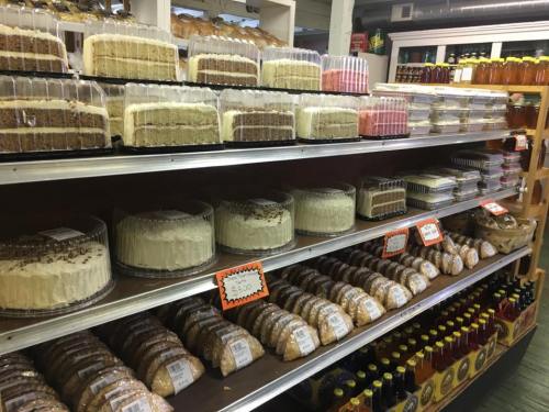 A bakery display featuring various cakes and cookies on shelves, with jars of honey in the background.