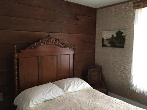 Cozy bedroom with a wooden bed, patterned wallpaper, and a framed landscape painting on the wall.