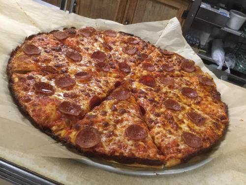 A large pepperoni pizza with melted cheese, sliced into wedges, on a parchment-lined baking tray.