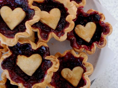 A close-up of heart-shaped jam tarts with a flaky crust and a glossy berry filling.