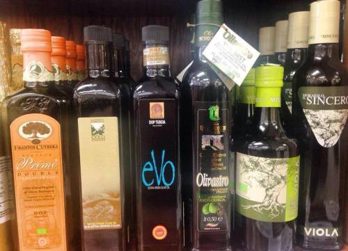A variety of olive oil bottles displayed on a shelf, featuring different brands and labels.