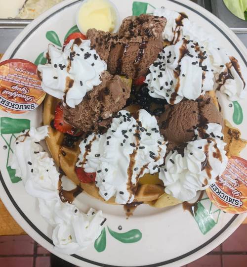 A plate of waffles topped with chocolate and vanilla ice cream, whipped cream, strawberries, and chocolate drizzle.