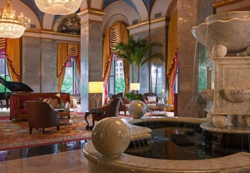 Luxurious hotel lobby featuring elegant furnishings, a fountain, and large windows with natural light.