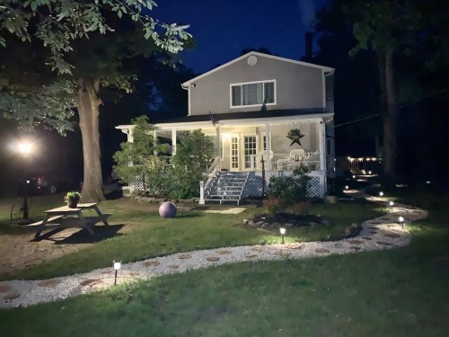 A well-lit house at night, surrounded by a landscaped yard with a winding path and decorative lights.