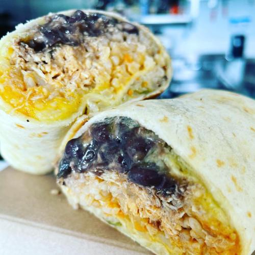 A close-up of a burrito cut in half, revealing layers of rice, beans, cheese, and shredded chicken inside a tortilla.