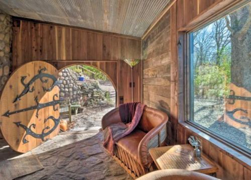 Cozy interior of a rustic cabin with wooden walls, a leather couch, and a large decorative door. Natural light from a window.