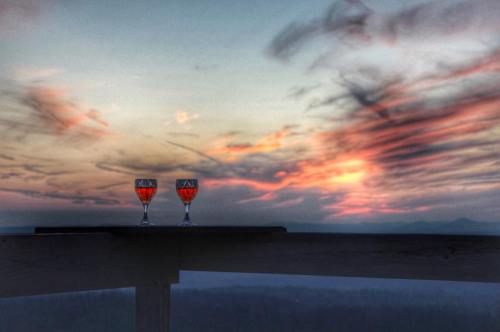 Two glasses of red drink sit on a table against a colorful sunset sky with wispy clouds.