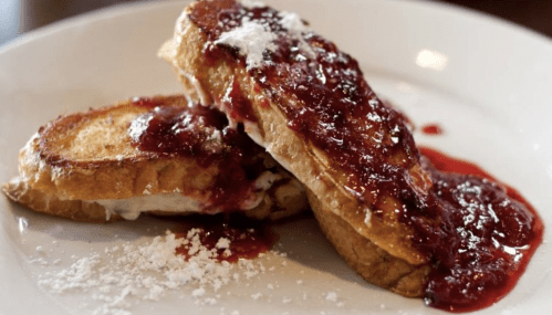 Two slices of French toast topped with berry sauce and powdered sugar on a white plate.