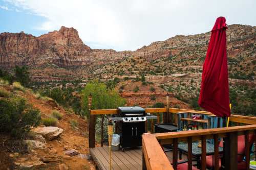 A scenic view from a deck featuring a grill, red umbrella, and mountains in the background.