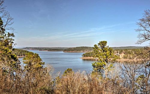A serene lake surrounded by trees under a clear blue sky, with distant hills visible on the horizon.