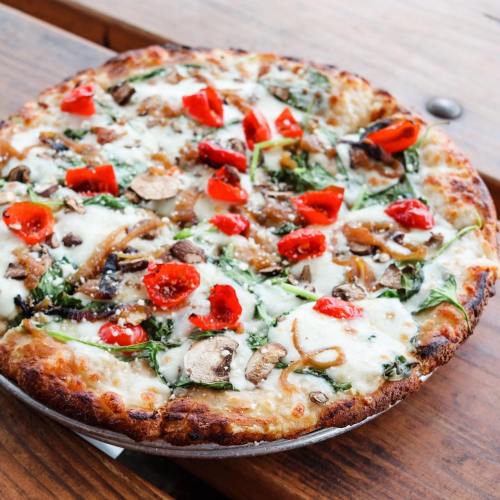 A freshly baked pizza topped with mushrooms, spinach, red peppers, and melted cheese on a golden crust.