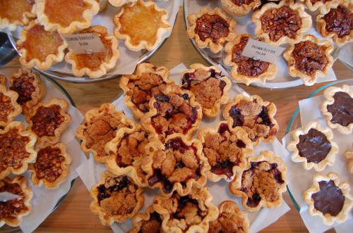 A variety of small, decorative pies on display, featuring different fillings like fruit, nuts, and chocolate.