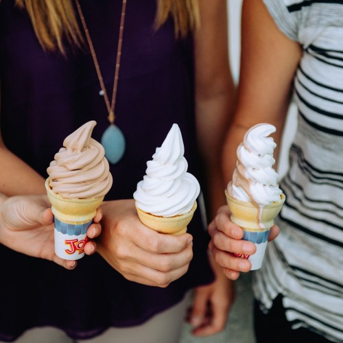 Three hands holding ice cream cones: one chocolate, one vanilla, and one swirl, against a casual background.