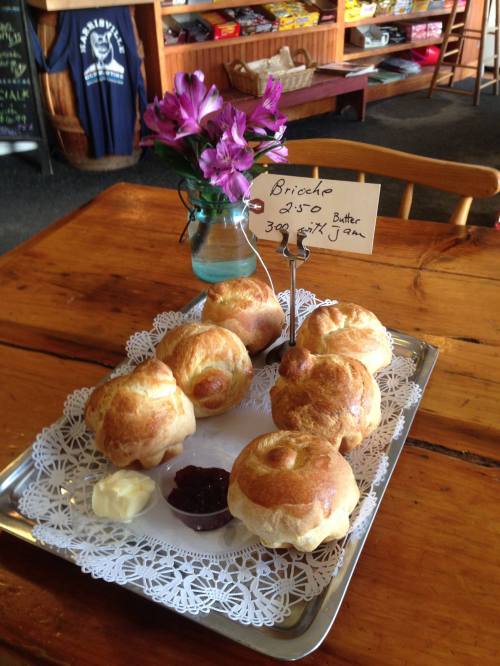 A plate of freshly baked brioche rolls with butter and jam, accompanied by a vase of flowers on a wooden table.