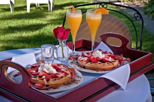 A breakfast tray with two waffles topped with strawberries and whipped cream, alongside two mimosas and a rose.
