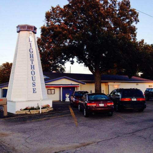 A lighthouse-shaped building with "LIGHTHOUSE" written on it, surrounded by trees and parked cars.