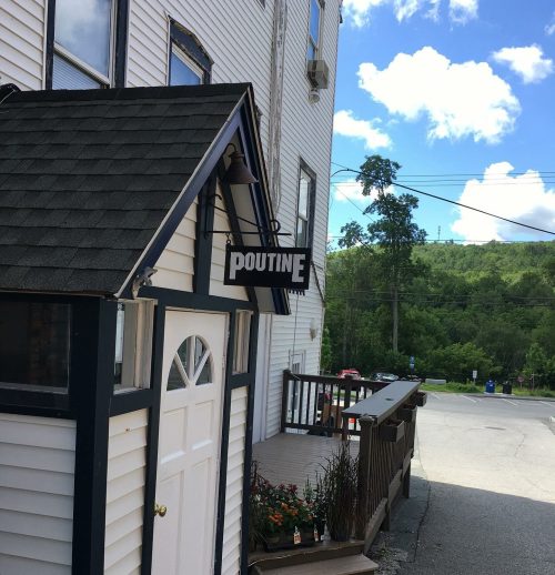 A small building with a sign reading "Poutine," surrounded by greenery and a clear blue sky.