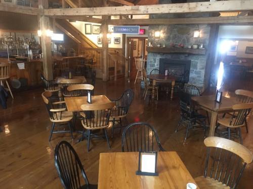 Cozy restaurant interior with wooden tables, chairs, a stone fireplace, and a bar area in a rustic setting.
