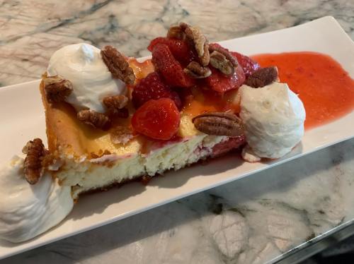 A slice of cheesecake topped with strawberries, raspberries, whipped cream, and pecans on a white plate.
