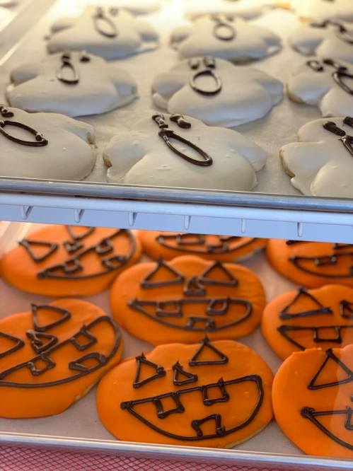 A display of Halloween-themed cookies: white ghost-shaped cookies and orange pumpkin-shaped cookies with chocolate details.
