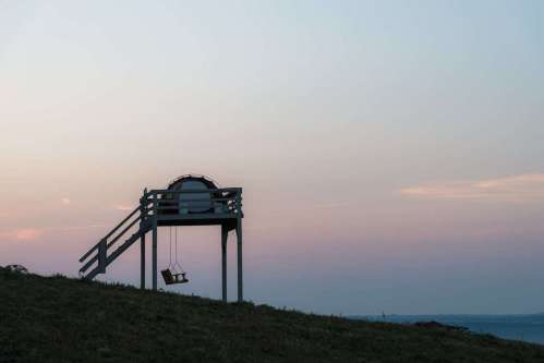 A wooden swing set on a hill against a pastel sunset sky.