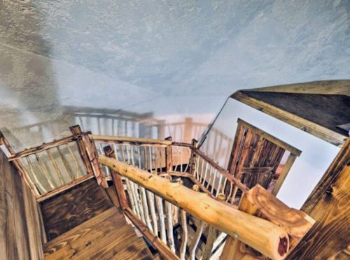 A wooden staircase with rustic railings, leading to a landing and a door, viewed from above.