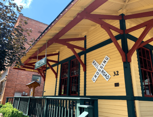 A bright yellow building with red accents, featuring a sign that reads "Shady" and a railroad crossing sign.