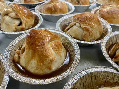 Golden-brown baked pastries in aluminum pie tins, filled with fruit and drizzled with syrup.