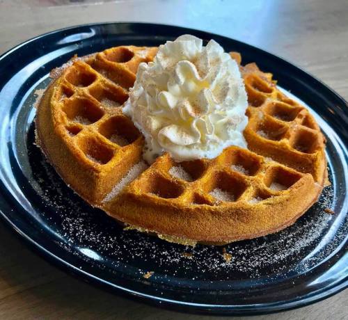 A golden-brown waffle topped with whipped cream, served on a black plate.