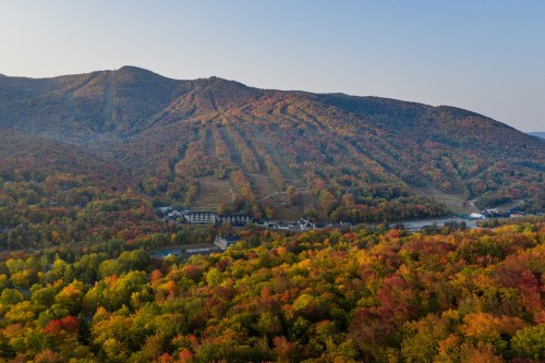 Aerial view of a colorful autumn landscape with mountains and a valley filled with vibrant fall foliage.