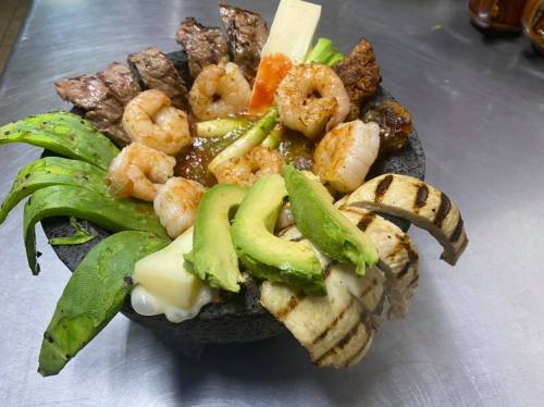 A vibrant dish featuring grilled shrimp, steak, avocado, and vegetables served in a stone bowl.
