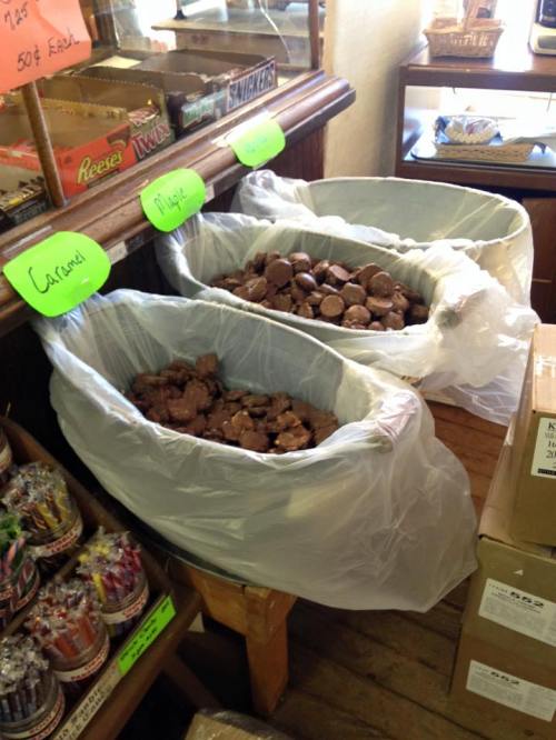 Three large bins filled with assorted chocolate treats, labeled "Caramel," "Maple," and "Other," in a candy shop.