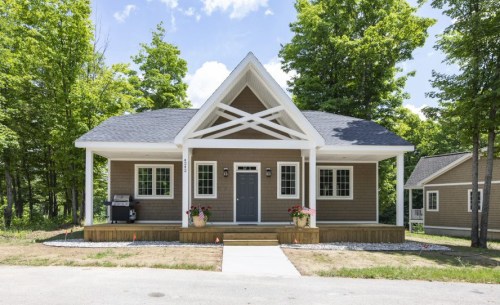 A charming single-story house with a front porch, surrounded by green trees and a clear blue sky.