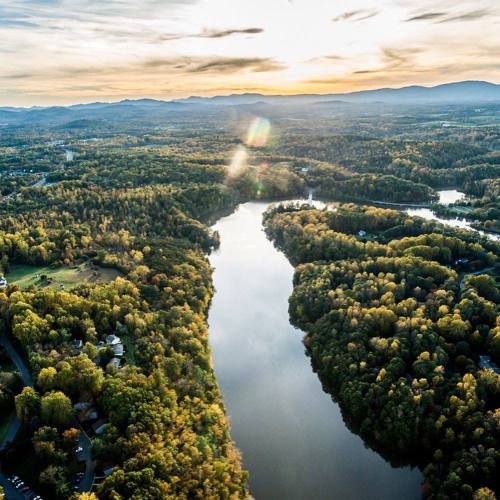 Aerial view of a winding river surrounded by lush, colorful trees under a sunset sky.