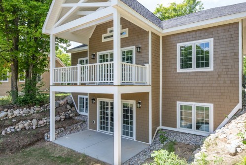 A modern two-story house with a balcony, large windows, and a landscaped yard.