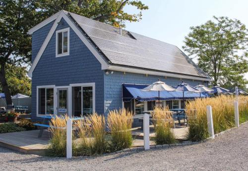 A blue cottage-style building with a sloped roof, surrounded by tall grass and outdoor seating under blue umbrellas.