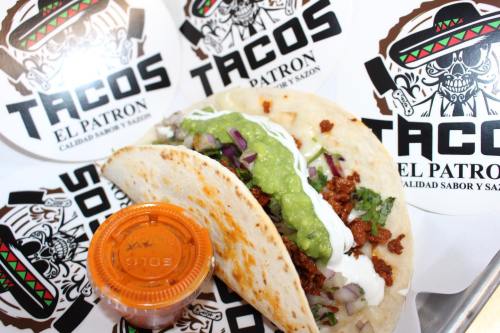 A delicious taco filled with meat, onions, and green sauce, served with a side of salsa, on a branded paper background.