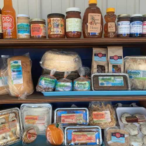 A display of various jars and packaged goods, including honey, sauces, and baked items on wooden shelves.