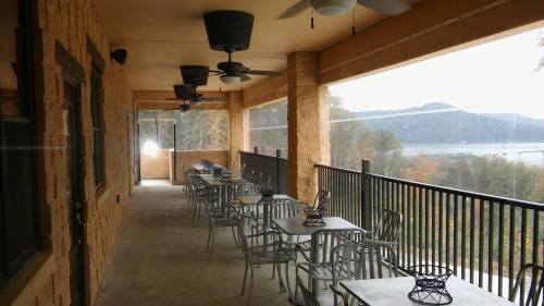 A covered outdoor patio with metal tables and chairs, overlooking a scenic view of trees and a body of water.