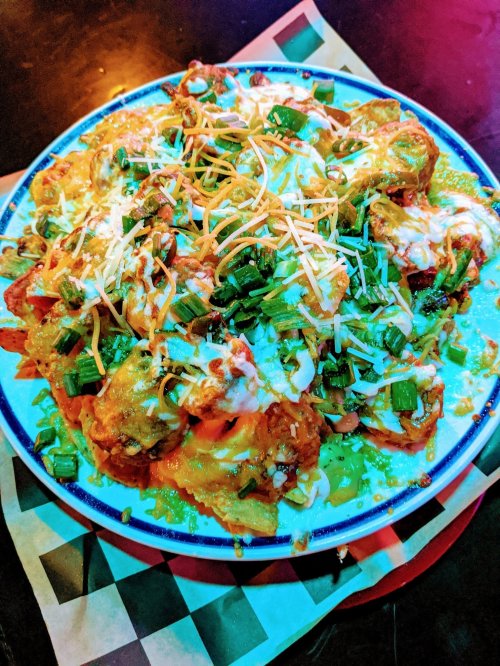 A colorful plate of nachos topped with cheese, green onions, and a drizzle of sauce, served on a checkered paper.