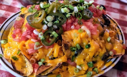 A plate of nachos topped with melted cheese, jalapeños, diced tomatoes, and green onions on a checkered tablecloth.