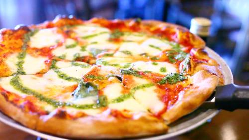 A freshly baked pizza topped with mozzarella, pesto, and fresh basil, served on a metal tray.