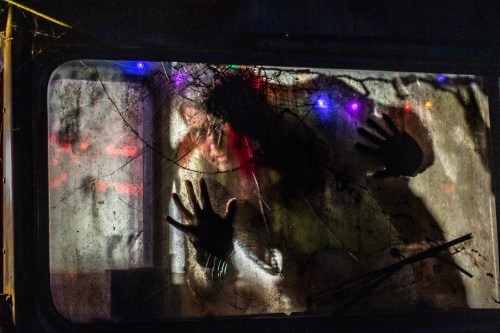 A figure presses against a foggy window, hands outstretched, with colorful lights glowing in the background.