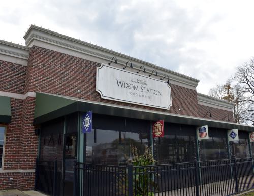 Exterior of Wixom Station restaurant, featuring a brick facade and large sign, with a cloudy sky above.
